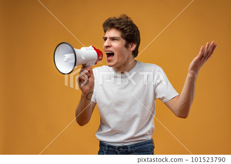 Young man shouting into megaphone making announcement against yellow background 101523790