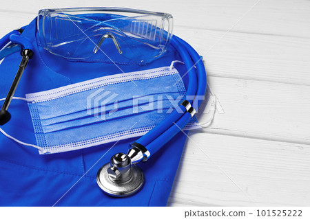 Doctor medical uniform with stethoscope and face mask on white wooden background Doctor medical uniform with stethoscope and face mask on white wooden background 101525222