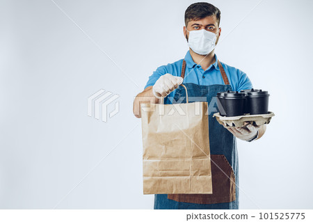 Delivery man in protective mask and medical gloves holding takeaway food. Compliance with the hygiene rules while covid-19 pandemic 101525775