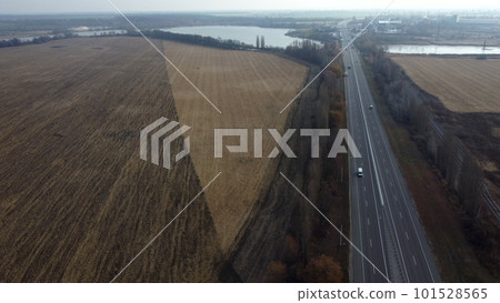 Large plowed field with plowed land and yellow dry straw after harvesting wheat, a lake, a highway with driving cars on an autumn day. Agro industrial agricultural farm landscape. Aerial drone view. Large plowed field with plowed land and yellow dry straw after harvesting wheat, a lake, a highway with driving cars on an autumn day. Agro industrial agricultural farm landscape. Aerial drone view. 101528565
