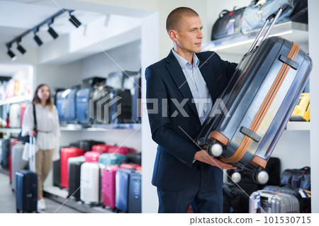 Confident man in a store carefully examines a travel suitcase Confident man in a store carefully examines a travel suitcase 101530715