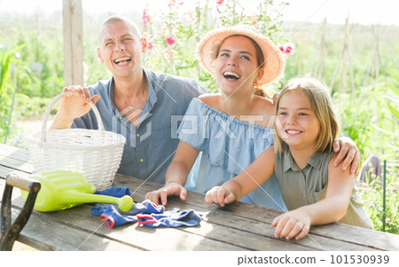 Happy family sits at table in backyard of summer cottage Happy family sits at table in backyard of summer cottage 101530939