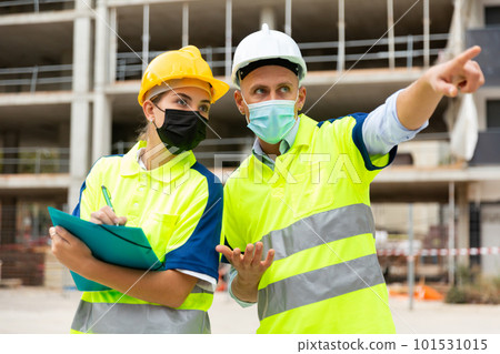Two engineers in protective masks are discussing a construction plan Two engineers in protective masks are discussing a construction plan 101531015