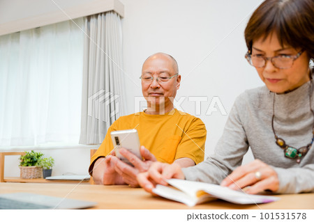 Two couples, an elderly man wearing reading glasses and operating a mobile phone, and an elderly woman reading a book Two couples, an elderly man wearing reading glasses and operating a mobile phone, and an elderly woman reading a book 101531578