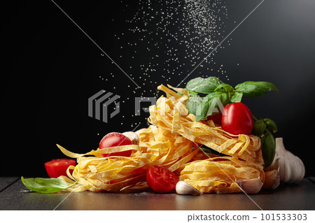 Homemade raw pasta with tomato, garlic, and basil on a black background. 101533303