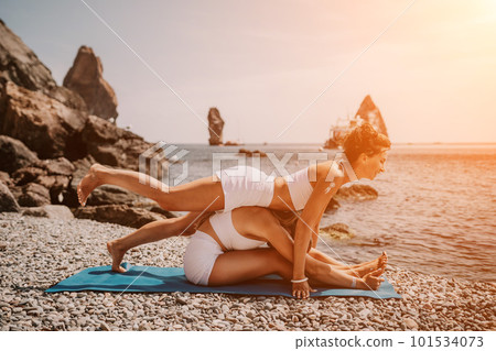 Woman sea yoga. Two Happy women meditating in yoga pose on the beach, ocean and rock mountains. Motivation and inspirational fit and exercising. Healthy lifestyle outdoors in nature, fitness concept. Woman sea yoga. Two Happy women meditating in yoga pose on the beach, ocean and rock mountains. Motivation and inspirational fit and exercising. Healthy lifestyle outdoors in nature, fitness concept. 101534073
