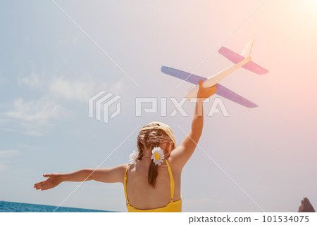 Kid playing with toy airplane. Children dream of travel by plane. Happy child girl has fun in summer vacation by sea and mountains. Outdoors activities at background of blue sky. Lifestyle moment. 101534075
