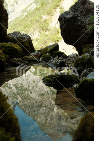 The Leogang mountains are reflected in the crystal clear water of the spring at the Birnbachloch near Leogang, Austria 101534129