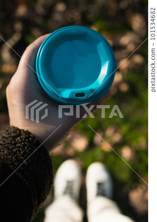 a glass with takeaway coffee in hands, against the background of blurry autumn leaves, top view 101534682