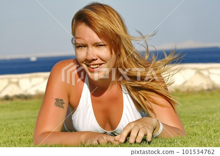red-haired young woman lying on the grass in a white swimsuit red-haired young woman lying on the grass in a white swimsuit 101534762