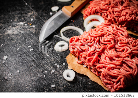 Fresh minced meat on paper on a table with a knife and onion rings. Fresh minced meat on paper on a table with a knife and onion rings. 101538662