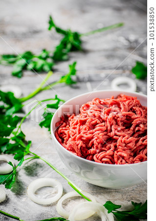 Minced meat in a bowl on a table with parsley and onion rings. Minced meat in a bowl on a table with parsley and onion rings. 101538850