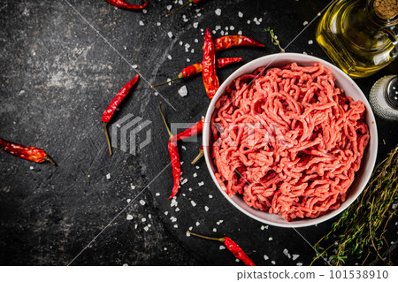 Minced meat in a bowl on a table with chili pepper pods. 101538910