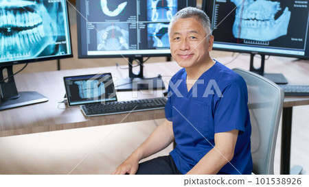 A senior man wearing a blue scrub who smiles in front of the monitor A senior man wearing a blue scrub who smiles in front of the monitor 101538926