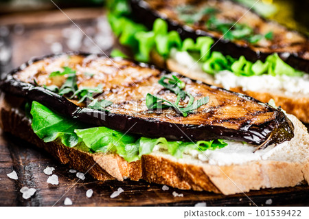 A fragrant sandwich with grilled eggplant on a cutting board. A fragrant sandwich with grilled eggplant on a cutting board. 101539422