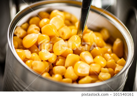 An open can of canned corn with a spoon. 101540161