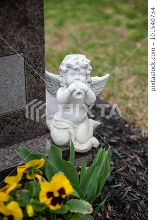 A small white angel statue plays a horn on a cemetery gravestone A small white angel statue plays a horn on a cemetery gravestone 101540734