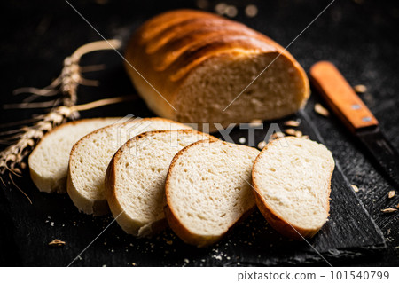 Sliced wheat bread with a knife on a stone board. 101540799