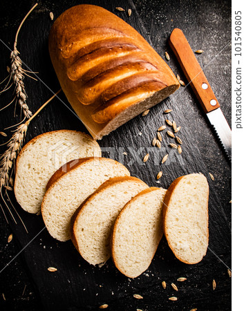 Sliced wheat bread with a knife on a stone board. 101540805