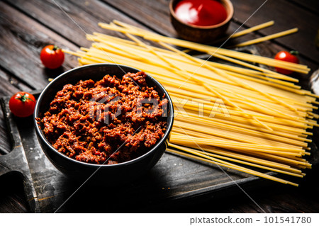 Bolognese sauce in a bowl on a cutting board with spaghetti dry. Bolognese sauce in a bowl on a cutting board with spaghetti dry. 101541780