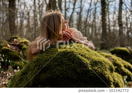 Snowdrops galanthus blond. A girl in a white dress lay down on a stone in the moss in a meadow with snowdrops in a spring forest 101542772