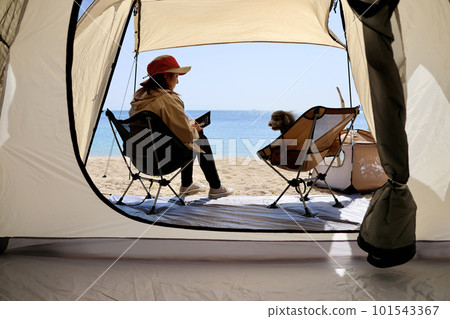 帶玩具貴賓犬的女子營地 蔚藍大海和美麗海灘上悠閒的海島營地 享受營地美食的女士 101543367
