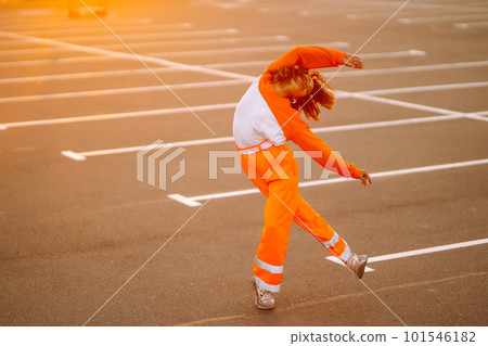 Young African American woman - dancer dancing in the street at sunset. Stylish woman with curly hair in an orange suit showing some moves. 101546182