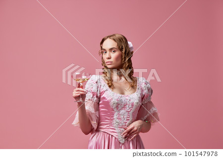 Shot of beautiful princess, queen wearing renaissance pink dress and standing with wine glass over studio background. Elegant lady with cocktail Shot of beautiful princess, queen wearing renaissance pink dress and standing with wine glass over studio background. Elegant lady with cocktail 101547978