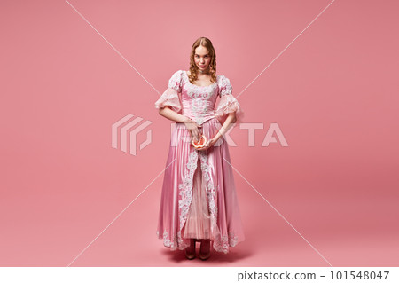 Portrait of young beautiful woman, princess wearing dress and holding grapefruit down with confident face over pink studio background. Female rights 101548047