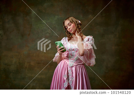 Portrait of beautiful blond princess wearing fancy pink dress and taking photo on cell phone over vintage texture background. Typical girl Portrait of beautiful blond princess wearing fancy pink dress and taking photo on cell phone over vintage texture background. Typical girl 101548120