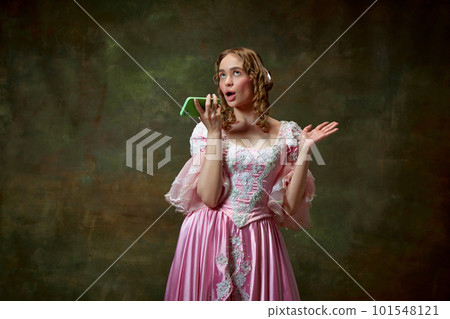 One charming blond princess wearing fancy pink dress and recording audio massage over vintage texture background. Gadgets in medieval age 101548121
