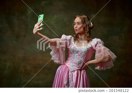 Portrait of beautiful blond princess wearing fancy pink dress and doing selfie on tablet over vintage texture background. Duck lips selfie Portrait of beautiful blond princess wearing fancy pink dress and doing selfie on tablet over vintage texture background. Duck lips selfie 101548122