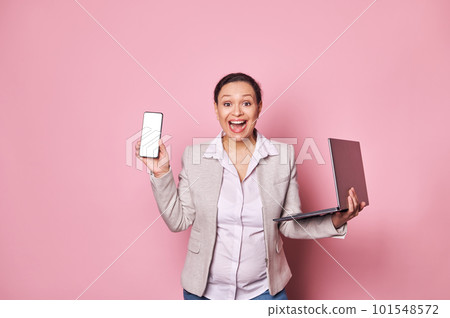 Excited pregnant business lady expressing amazement, looking at camera, holding laptop and smartphone with white blank screen, with free ad space for mobile applications, isolated over pink background 101548572