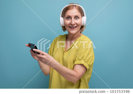 portrait of a blond adult woman with headphones and a smartphone in her hands portrait of a blond adult woman with headphones and a smartphone in her hands 101553596