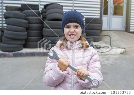 Portrait of a child holding a wrench in his hands, against the background of a garage. Portrait of a child holding a wrench in his hands, against the background of a garage. 101553733