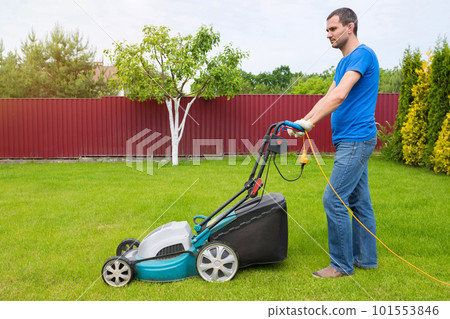 Worker with a lawn mower mows grass in the garden. Side view 101553846