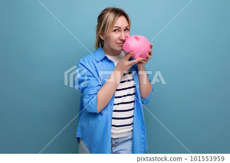 blond smiling girl in casual outfit holding a piggy bank on a blue background with copy space blond smiling girl in casual outfit holding a piggy bank on a blue background with copy space 101553959