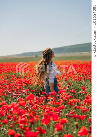 Happy woman in a poppy field in a white shirt and denim skirt with a wreath of poppies on her head posing and enjoying the poppy field. 101554096