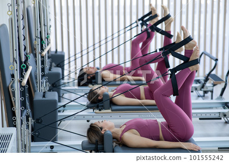 Three Asian women in pink sportswear doing pilates exercises with a reformer bed. Three Asian women in pink sportswear doing pilates exercises with a reformer bed. 101555242