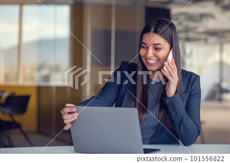 Serious businesswoman talking on mobile phone at office workplace, working at computer. Secretary answering telephone call. 101556822