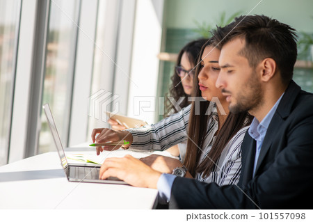 Creative business team sharing laptop in office, watching startup presentation, brainstorming, pointing at monitor, talking. 101557098