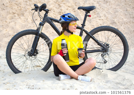 Beautiful woman cyclist in yellow with tea and thermos in hand on the background of sand Beautiful woman cyclist in yellow with tea and thermos in hand on the background of sand 101561376