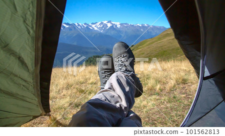 leg tourist in boots out of the tent with mountains in the background 101562813