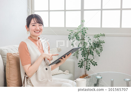A smiling Japanese woman sitting on a sofa at home and doing online shopping, reading, and doing side jobs on a tablet device A smiling Japanese woman sitting on a sofa at home and doing online shopping, reading, and doing side jobs on a tablet device 101565707