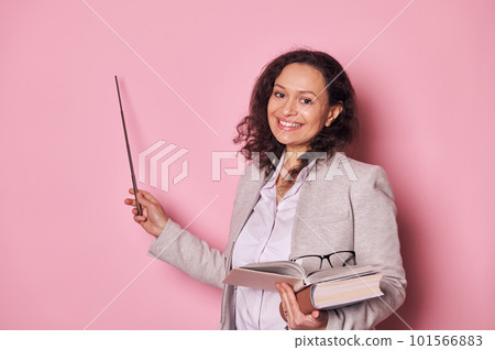 Cheerful experienced middle aged female teacher in casual clothes, pointing with pointer at copy advertising space on pink background, smiling looking at camera while explaining lesson 101566883