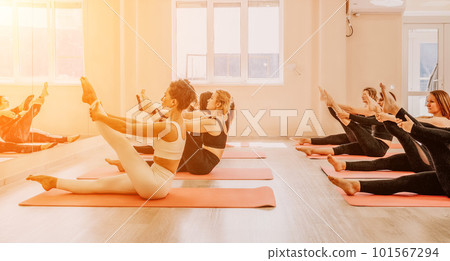 Group of happy middle aged women with fitness instructor, stretching in the gym before pilates, on a yoga mat near the large mirror. Female fitness yoga routine concept Group of happy middle aged women with fitness instructor, stretching in the gym before pilates, on a yoga mat near the large mirror. Female fitness yoga routine concept 101567294