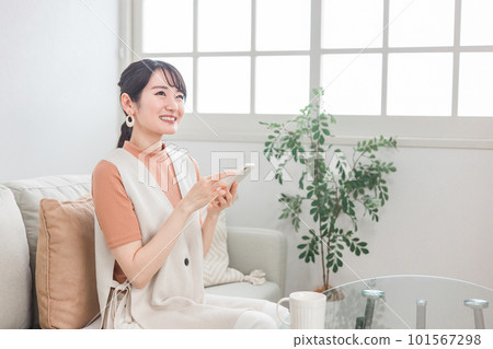 日本女性在家沙發上使用智能手機進行網上購物、閱讀、副業 101567298