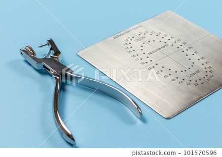 Dental hole punch and the metal plate on the blue. Dental hole punch and the metal plate on the blue. 101570596