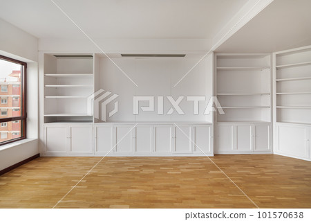 Empty built-in white cabinet on wooden laminate floor with big window in empty bright airy room in housewarming. Concept of housewarming and convenient storage Empty built-in white cabinet on wooden laminate floor with big window in empty bright airy room in housewarming. Concept of housewarming and convenient storage 101570638