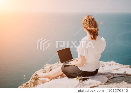 Woman sea laptop. Successful business woman working on laptop by the sea. Pretty lady typing on computer at summer day outdoors. Freelance, digital nomad, travel and holidays concept. Woman sea laptop. Successful business woman working on laptop by the sea. Pretty lady typing on computer at summer day outdoors. Freelance, digital nomad, travel and holidays concept. 101570840